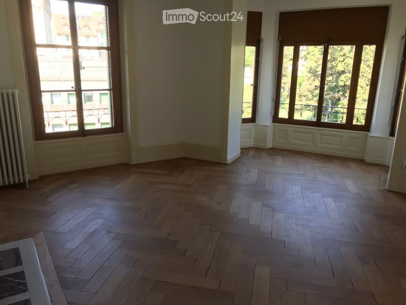 Empty room with wooden herringbone flooring, large windows with wooden frames, and white walls. No furniture or equipment present.