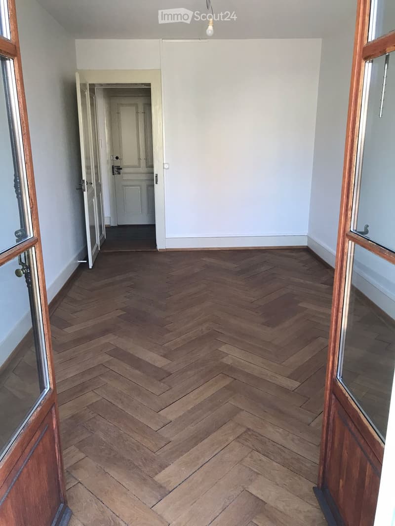 Empty hallway with wooden herringbone flooring, white walls, and open doors leading to other rooms.