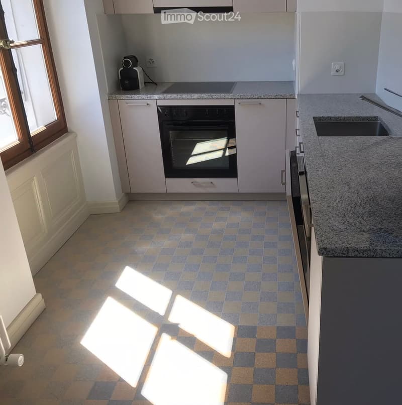 Modern kitchen with white cabinets, granite countertop, tiled floor, and built-in oven. Features a sink with a modern faucet and a coffee maker on the counter.