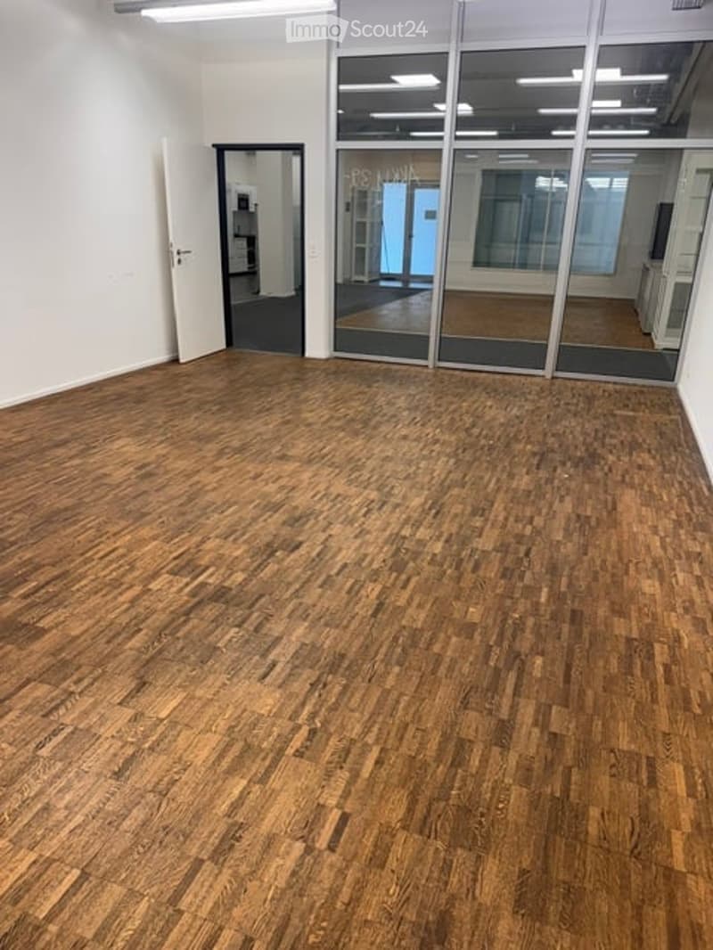 Empty room with wooden flooring, white walls, and large glass partitions. No furniture or equipment present.