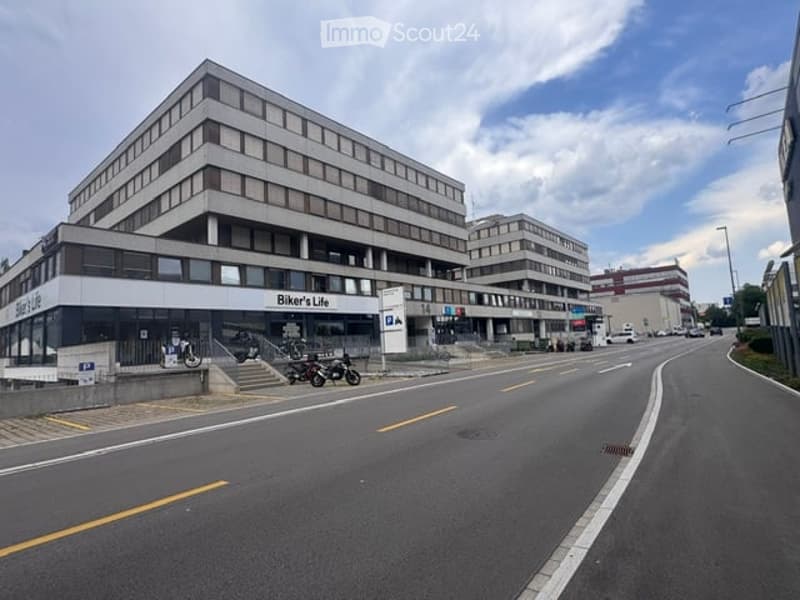 Multi-story commercial building with a storefront labeled "Biker's Life" and several motorcycles parked outside. The building has a modern design with large windows and a flat roof.