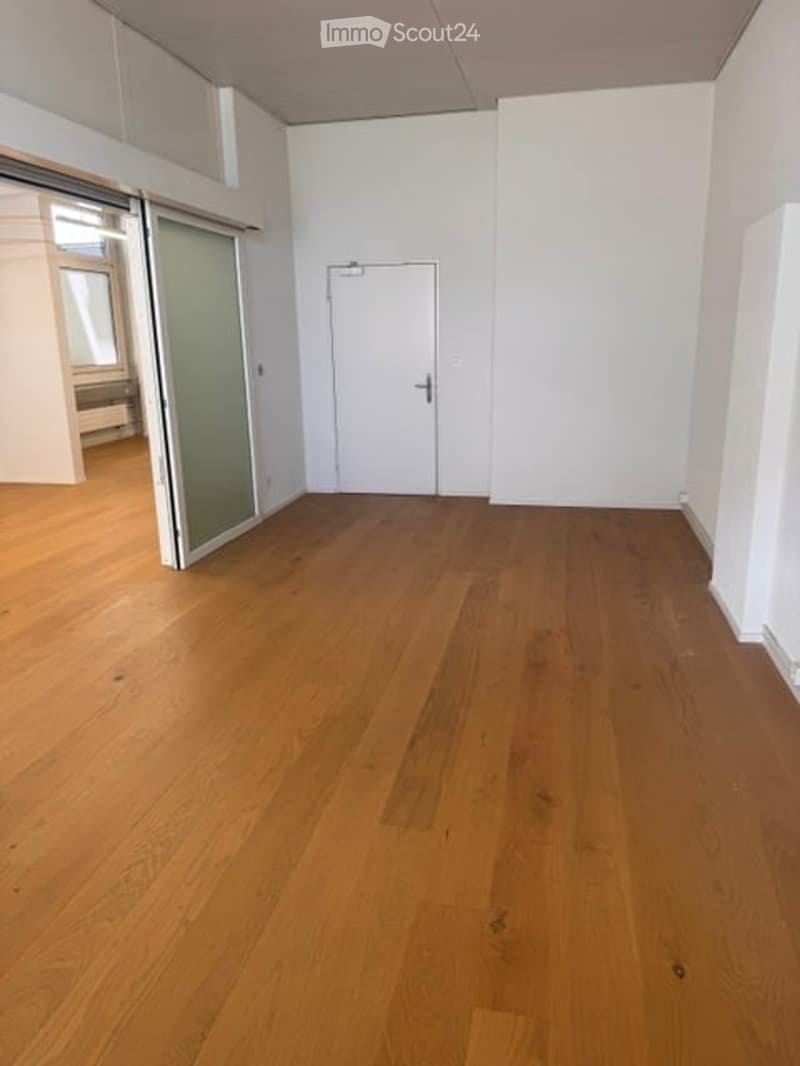 Empty room with wooden flooring, white walls, a white door, and a glass sliding door leading to another area.