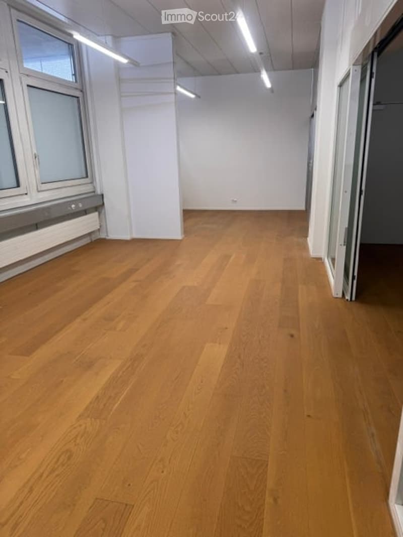 Completely empty room with wooden flooring, white walls, and large windows. No furniture or equipment.