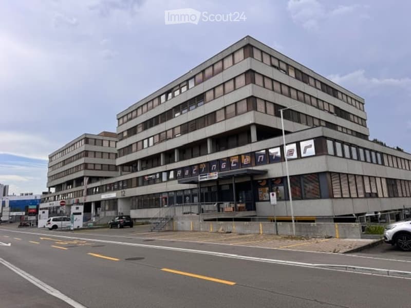 Modern multi-story building with a flat roof and large windows, featuring signage for "Razencenter" and a parking area in front.