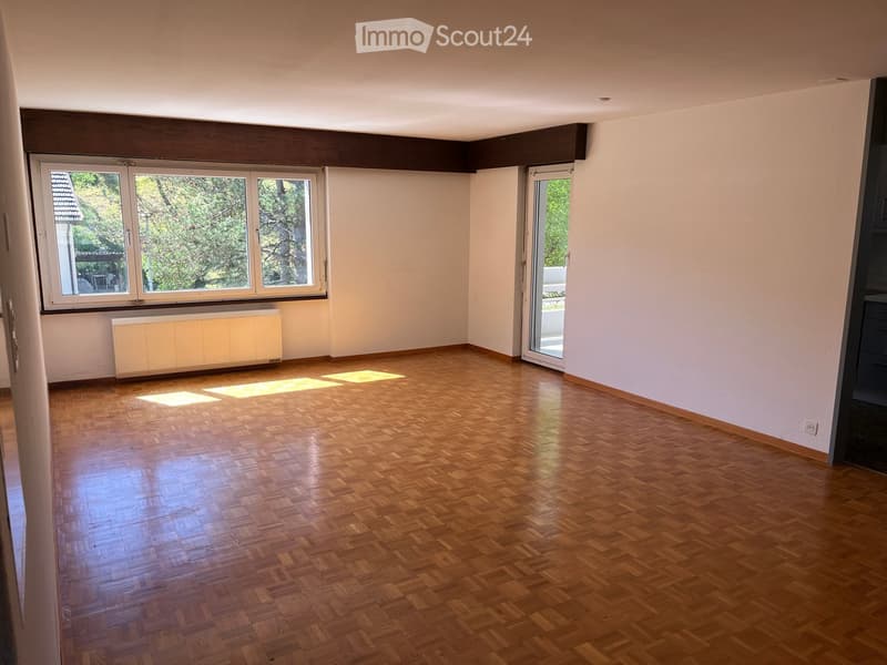 Empty room with wooden parquet flooring, large windows, and a radiator. No furniture or equipment present.