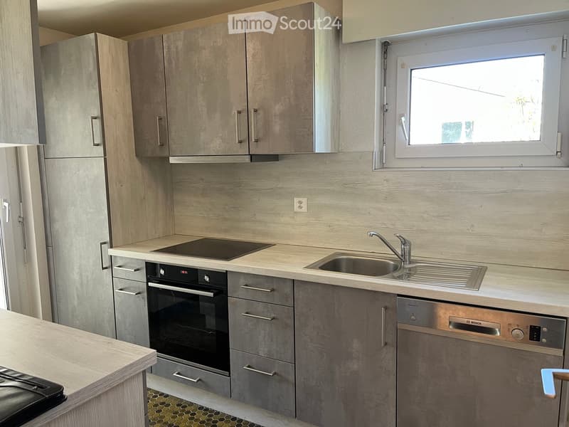 Modern kitchen with light wood cabinets, stainless steel appliances, and a window above the sink.