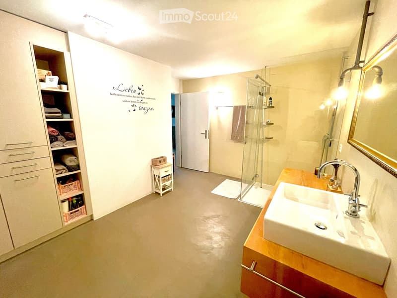 Modern bathroom with a double sink, large mirror, glass shower enclosure, built-in cabinet, and decorative wall quote.