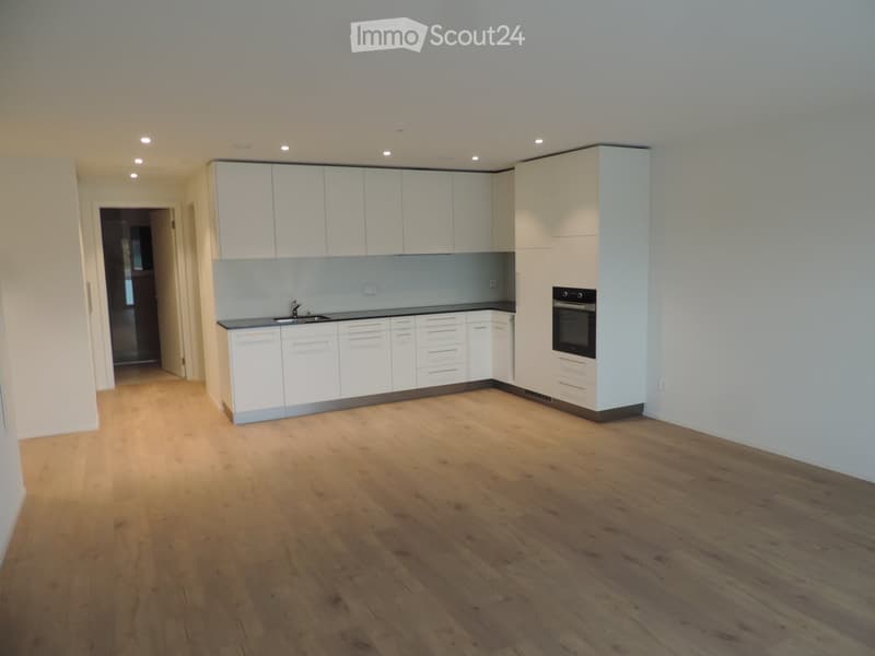 Empty kitchen with white cabinets, wooden flooring, and built-in appliances including an oven and sink.