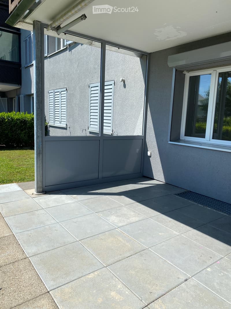 Concrete paved area, white ceiling, metal railing, large sliding doors, building with glass windows