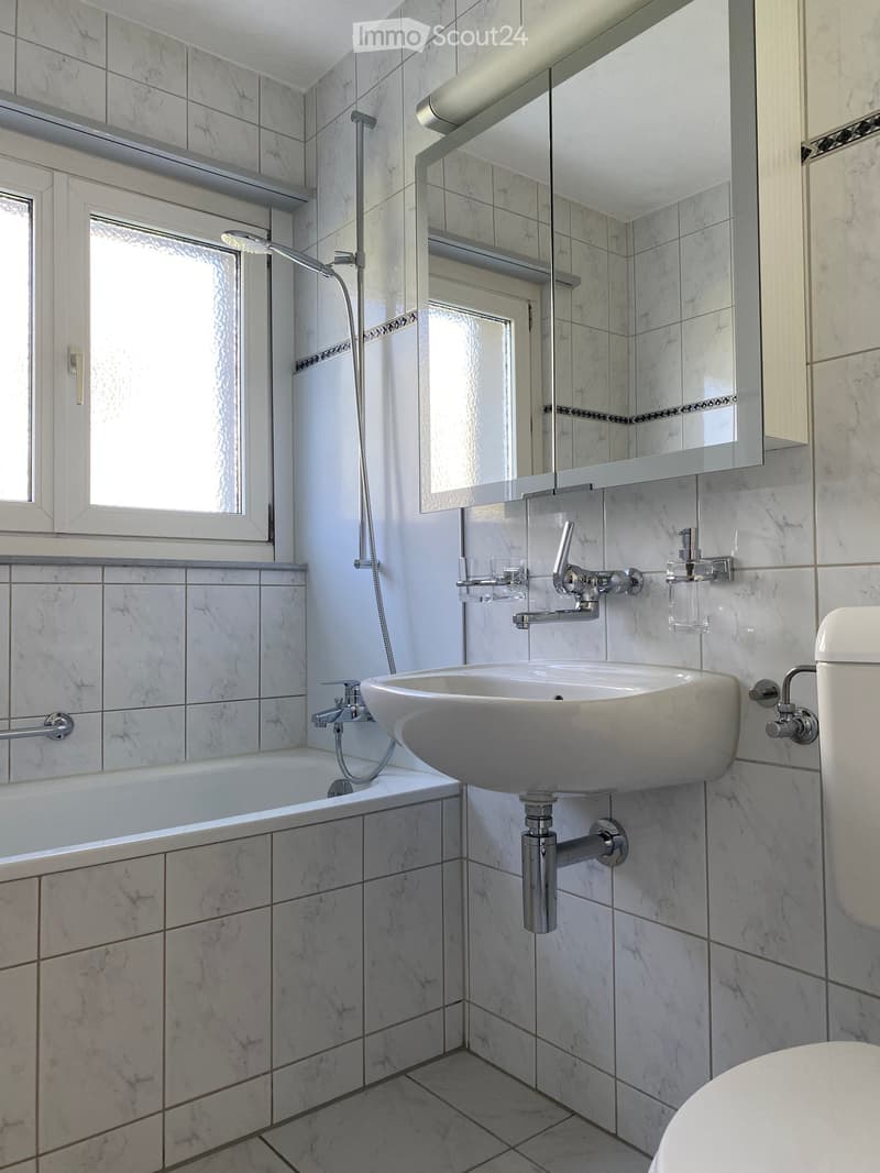 modern bathroom with white tiles, a white sink with silver fixtures, a white bathtub, a mirror with glass door, a toilet, and a shower head