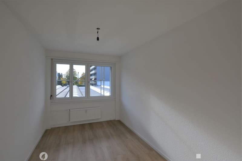 Empty room with white walls, wooden flooring, a single window, and a radiator. No furniture or equipment present.