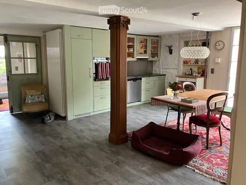 Furnished Room. A modern kitchen and dining area with light green cabinets, a central island, a dining table with chairs, and a dog bed on the floor.