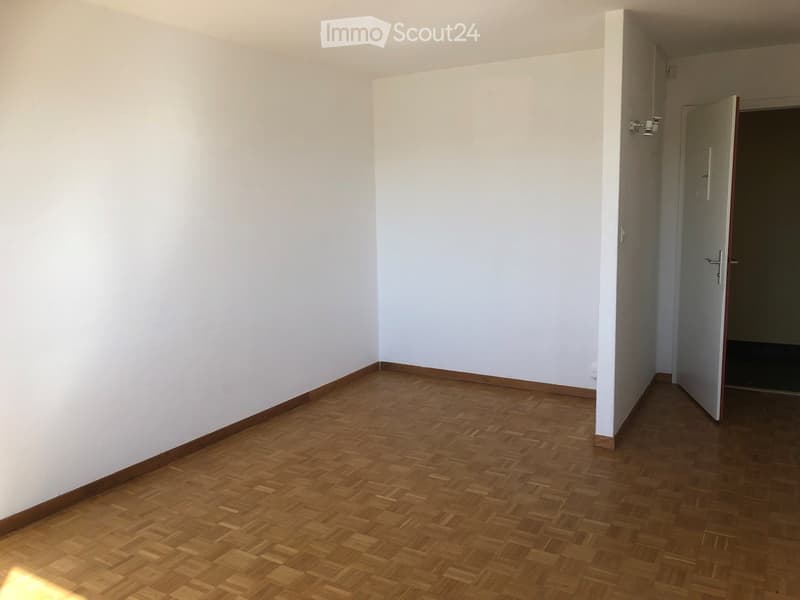 Empty room with wooden parquet flooring and white walls, featuring a doorway leading to another space.