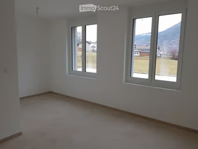 Empty room with white walls, wooden floor, and two windows offering a view of the outdoors.