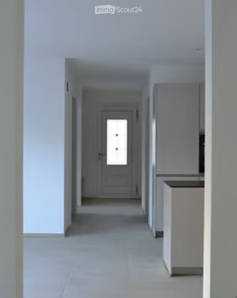 Empty hallway with white walls, grey door at the end, and a grey cabinet on the right side.