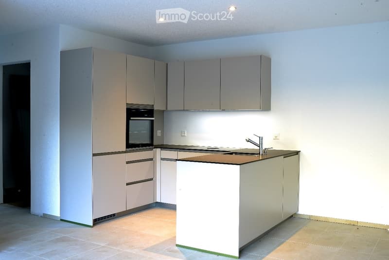 Modern kitchen with light grey cabinets, a central island, and built-in appliances including an oven and sink.
