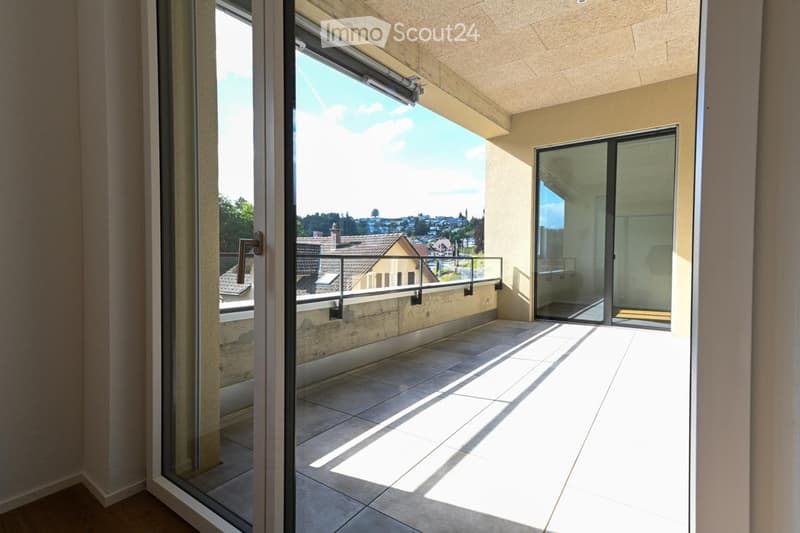 Spacious balcony with tiled floor, large glass sliding doors, and a view of the cityscape and rooftops.