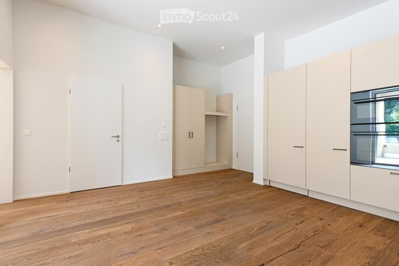 Empty room with light wooden flooring, white walls, and built-in cabinetry. No furniture or appliances present.
