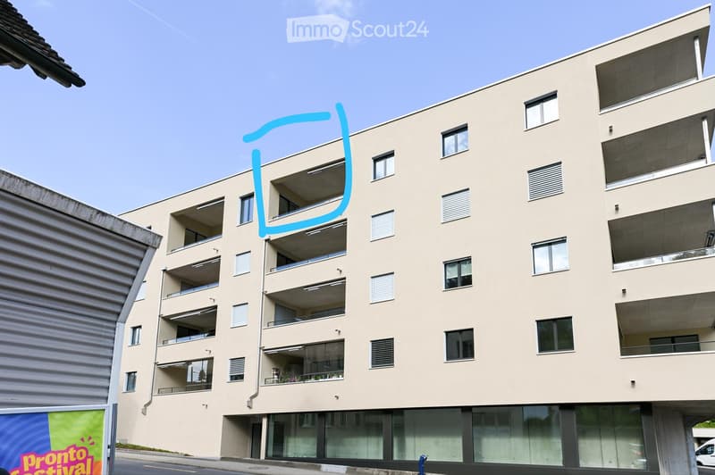 Modern multi-story residential building with beige facade, multiple balconies, and large windows. The building features contemporary design with clean lines and a flat roof.