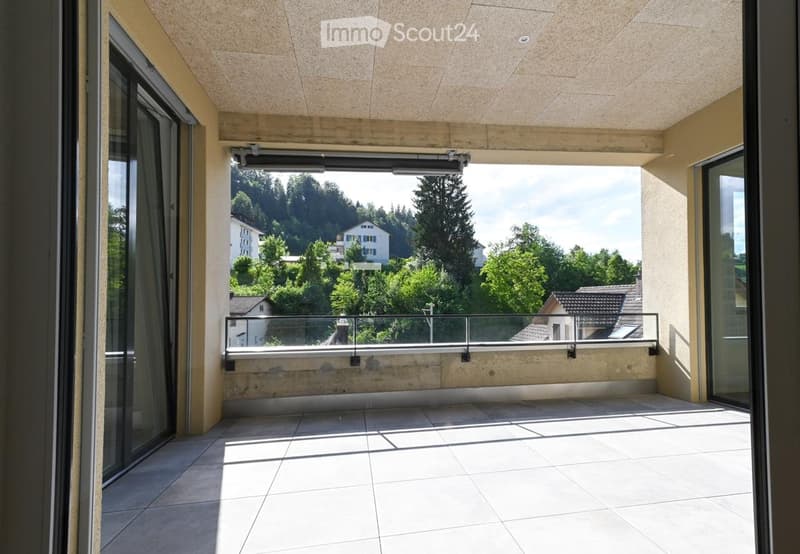 Modern balcony with tiled floor, glass balustrade, and scenic view of trees and houses.