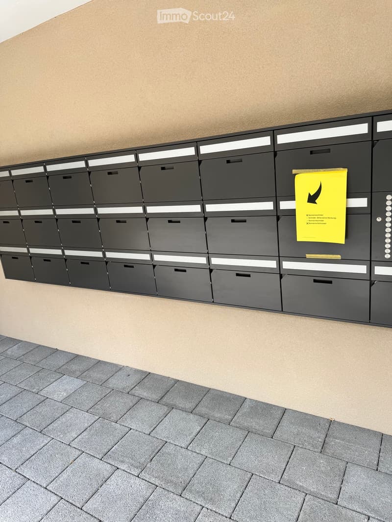 A modern hallway with a row of black mailboxes with white trim, a yellow waste disposal sign, and a gray tiled floor.
