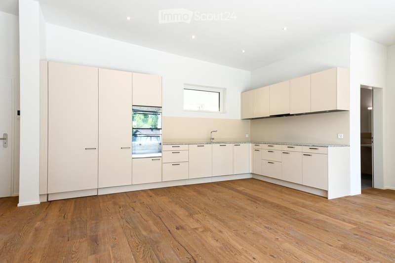 Modern kitchen with light-colored cabinets, wooden flooring, and a small window above the sink.