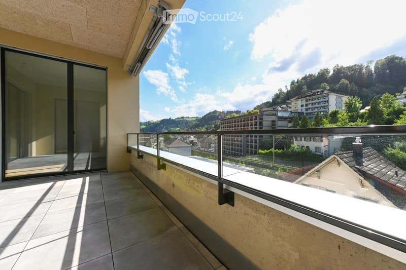 Balcony with tiled floor, glass railing, and scenic view of town and hills.