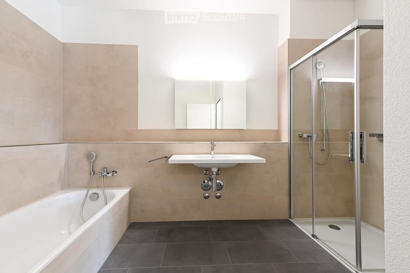 Modern bathroom with a bathtub, a wall-mounted sink, a large mirror, and a glass-enclosed shower stall. Light beige tiles and dark grey flooring.