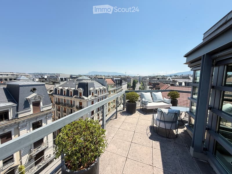 Balcony with a cityscape view, featuring a sofa, chairs, a small table, and potted plants.