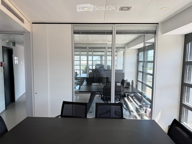 Modern office space with large glass partitions, black conference table, and several chairs.