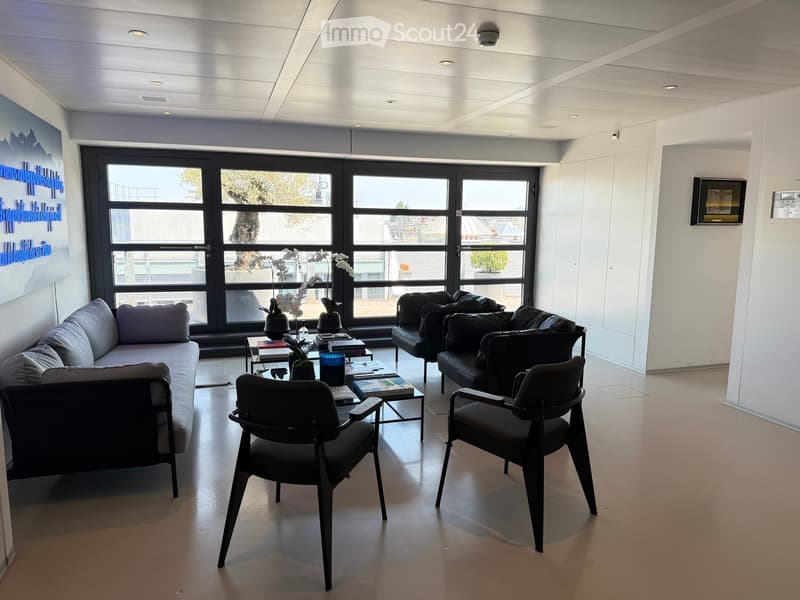 Modern living room with large windows, grey sofa, coffee table, black chairs, and decorative vases.