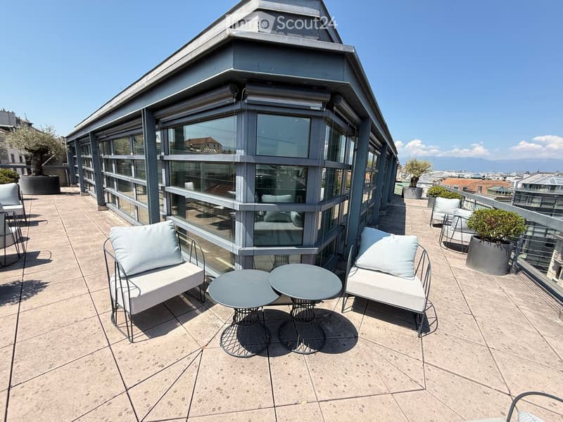 Modern rooftop terrace with a sofa, two round tables, and several chairs, surrounded by glass walls and a cityscape view.