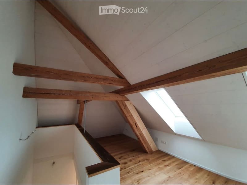 An attic space with exposed wooden beams, wooden flooring, and a skylight window allowing natural light to enter.
