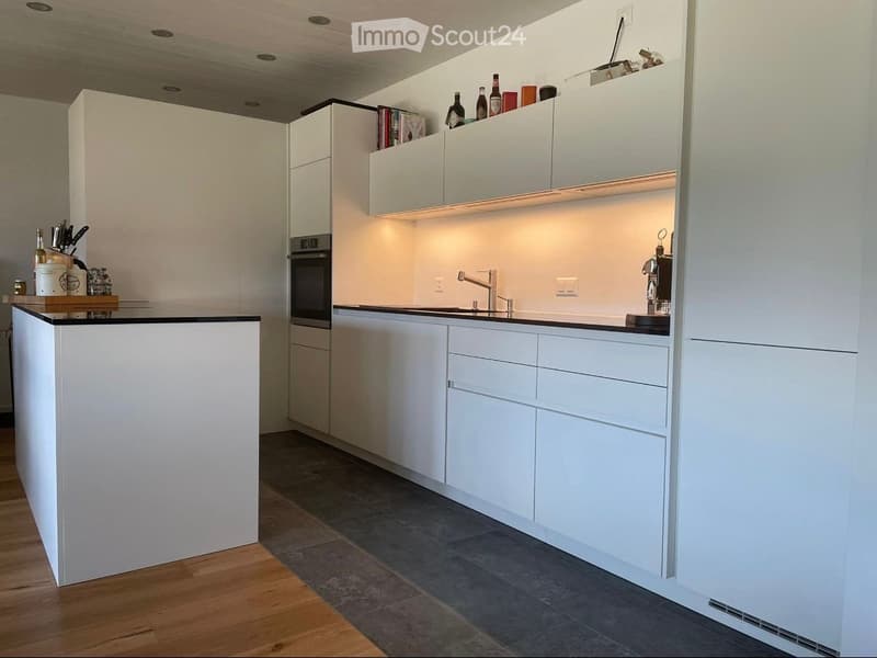 Modern kitchen with white cabinets, black countertops, and built-in appliances. Features include a central island, overhead lighting, and a sleek design.