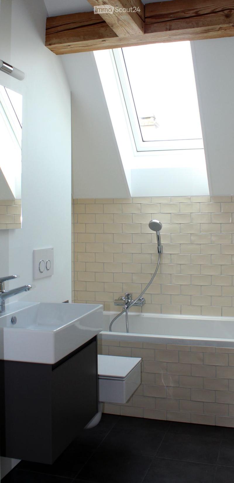 Modern bathroom with a white sink, bathtub, toilet, and showerhead. Light-colored tiles and a skylight window provide natural light.