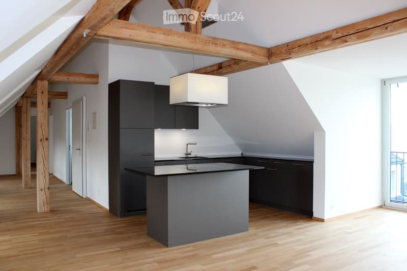 Modern kitchen with dark cabinets, a central island, wooden flooring, and exposed wooden beams on the ceiling.