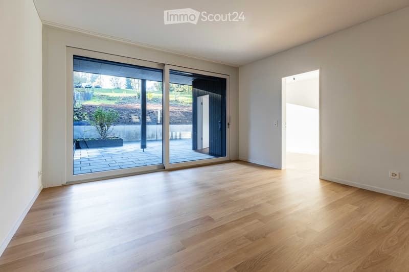 Empty room with hardwood floors, white walls, and large sliding glass doors leading to a patio.