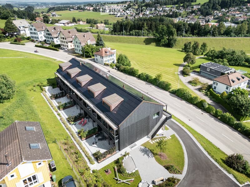 Modern building with a black exterior, solar panels on the roof, and a driveway leading to it.