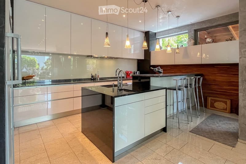 White cabinetry, black countertops, island with double sink, modern fixtures, ample storage, three barstools, wine bottle holder, rug, backsplash