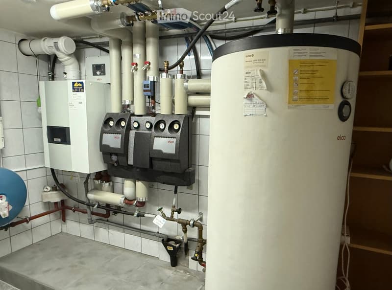 A basement with tiling, various heating and water pipes, and meters.
