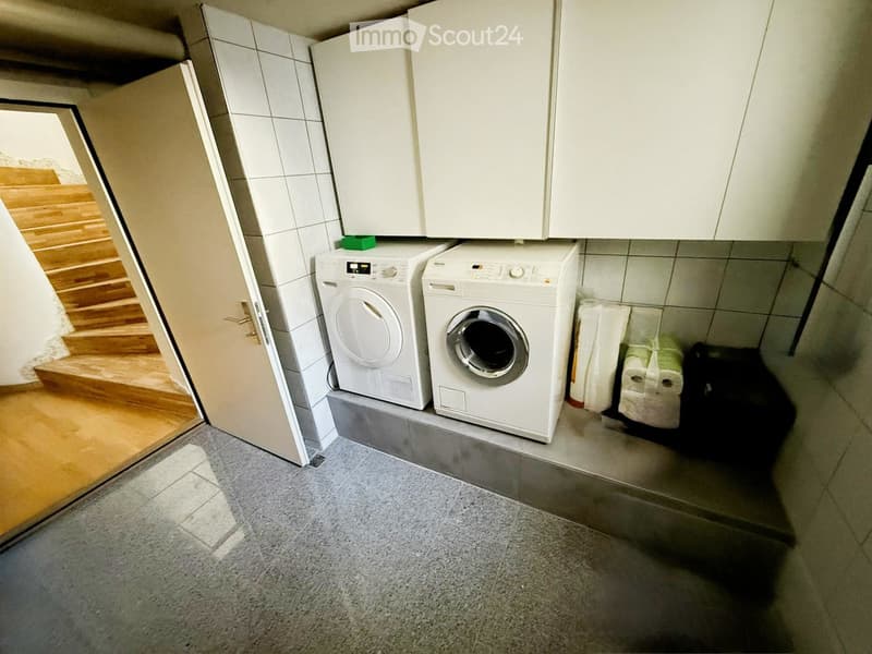 Compact bathroom with a washing machine and dryer, white tiled walls, and a small window letting in natural light.