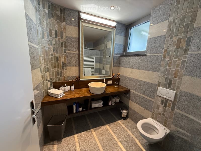 Large sink, marble countertop, floor-mounted mirror, under-mirror lighting, tile walls, towel racks, toilet, power outlet, trash bin