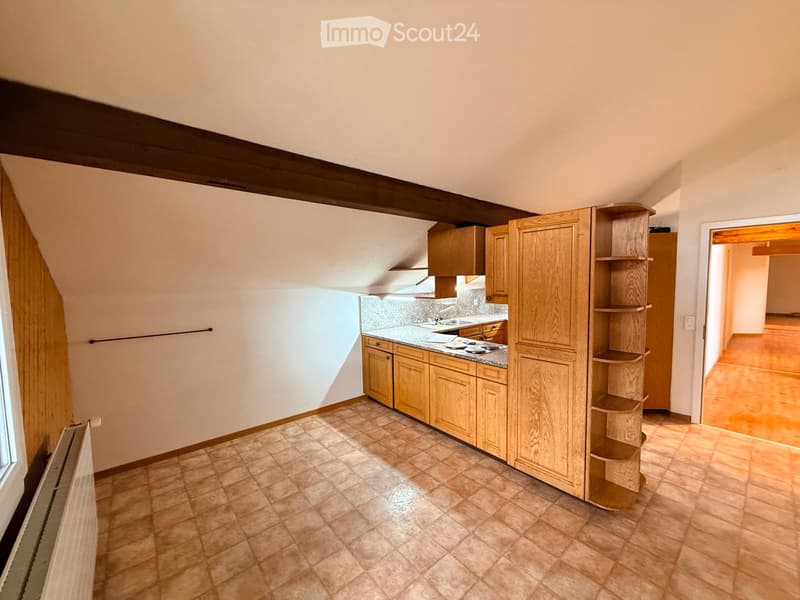 Bright kitchen with wooden cabinets, tiled floor, and a countertop with a sink and stove. Natural light streams in from a window on the left.