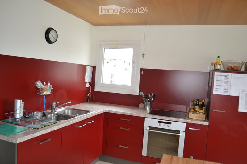 Modern kitchen with red cabinets, granite countertops, stainless steel sink, oven, and refrigerator. Features a window, clock, and various kitchen items on the counter.