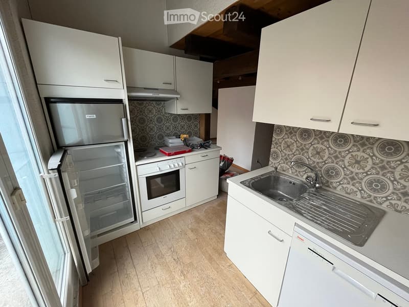 Modern kitchen with white cabinets, stainless steel sink, refrigerator, and oven. Features a decorative backsplash and wooden flooring.