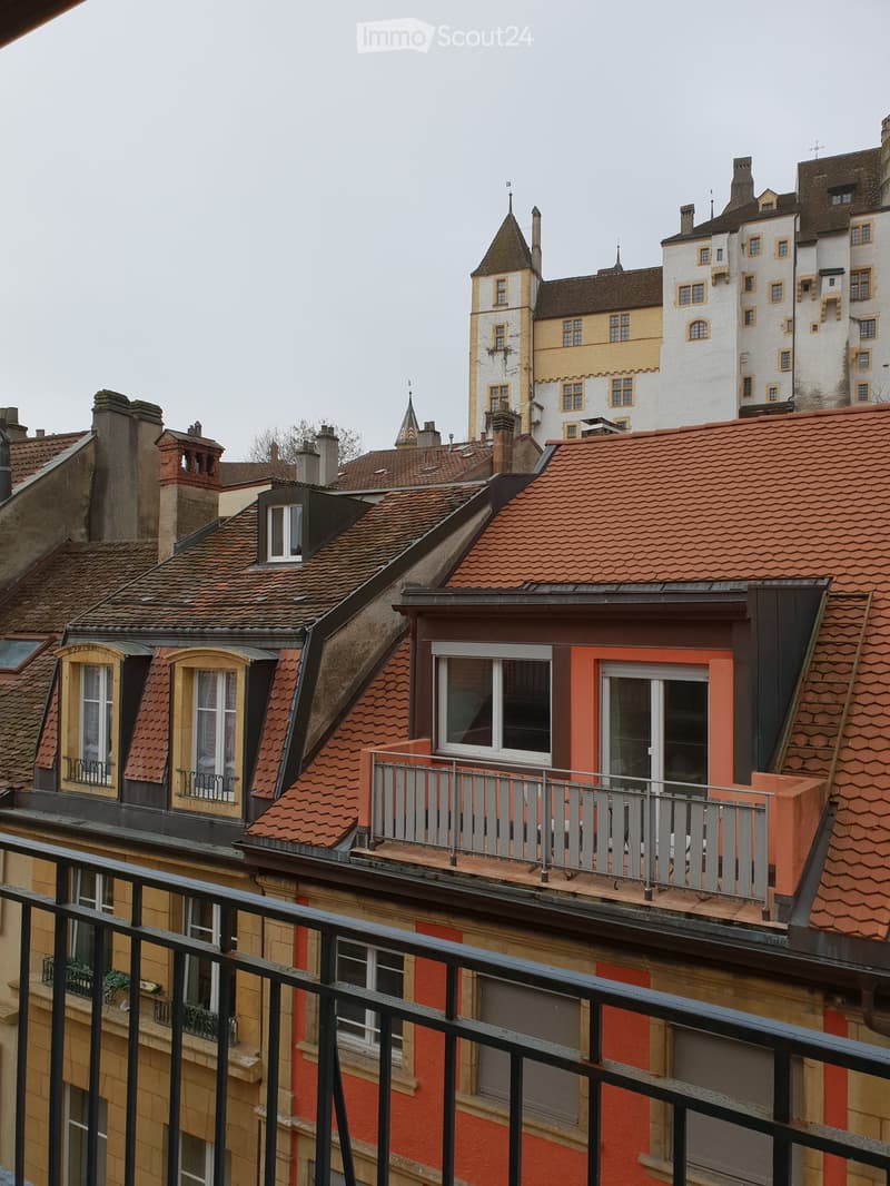 Balcony overlooking a historic cityscape with red-tiled roofs, chimneys, and ornate buildings.