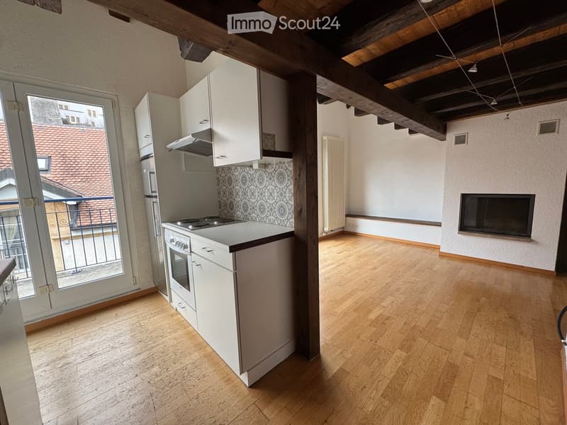 Open-plan kitchen and living area with wooden flooring, white kitchen cabinets, stove, oven, refrigerator, range hood, radiator, and fireplace.