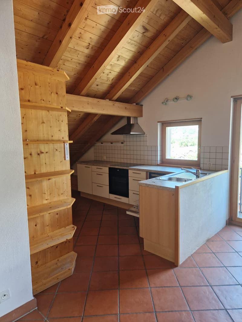 Bright kitchen with wooden beams, white cabinets, stainless steel sink, oven, and range hood. Natural light from a window illuminates the space.