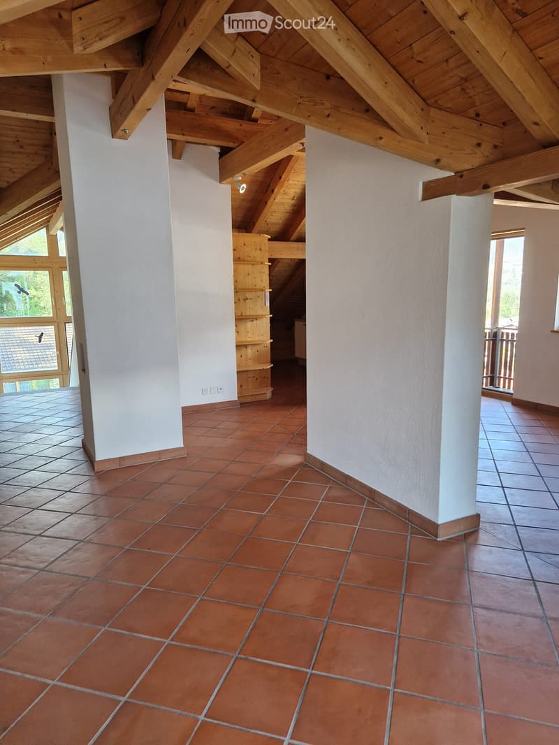Empty room with exposed wooden beams on the ceiling, red tiled floor, white walls, and large windows with wooden frames.