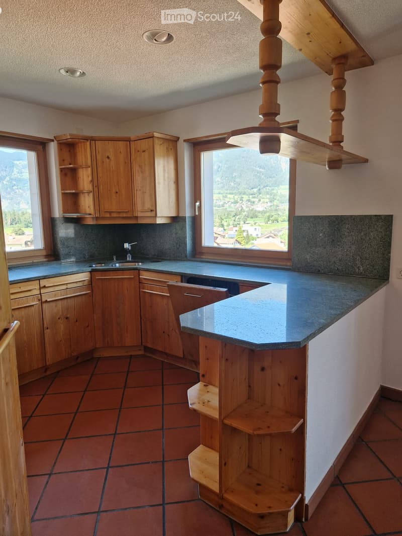 Kitchen with wooden cabinets, granite countertops, sink, and a wooden shelf. Large windows offer a scenic mountain view.
